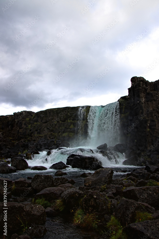 Fototapeta premium Waterfall flowing through the tectonic rift of UNESCO Thingvellir National Park, Iceland. Volcanic rocks and dramatic water movement symbolize natural forces, geological time and resilience.