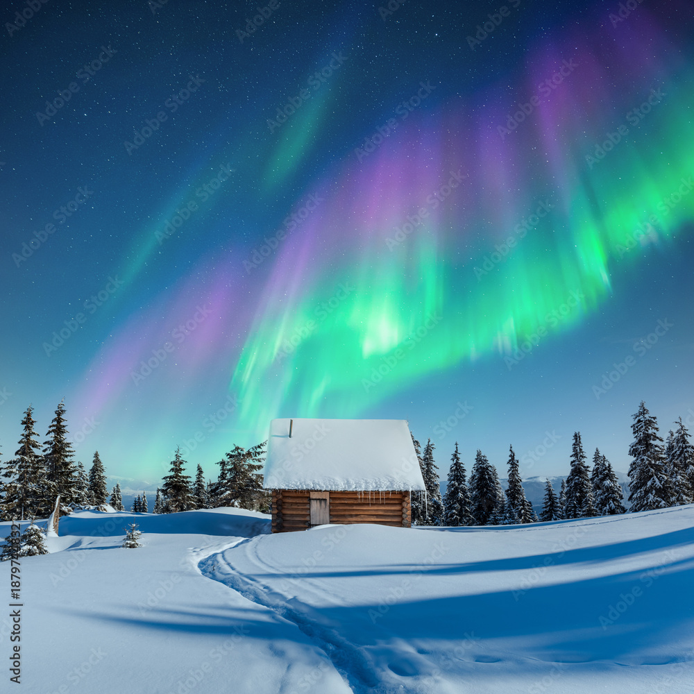 Fototapeta premium Cozy wooden hut in snowy mountains under incredible Northern lights in starry sky. Christmas landscape with Polar lights in winter time. Aurora Borealis