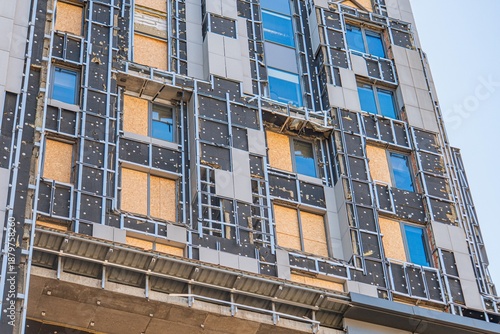 Under construction modern city building, metal beams, studs, gray concrete and steel structure, windows with glass panes or openings, black and silver color scheme, no text, bright daylight, construc