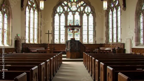 Empty wooden church pews face a pulpit with a cross, sunlight filtering through colorful stained glass windows in peaceful sanctuary