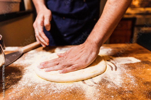 Fényképezés Baker's hands flatten sourdough dough on flour-dusted wooden cutting board durin