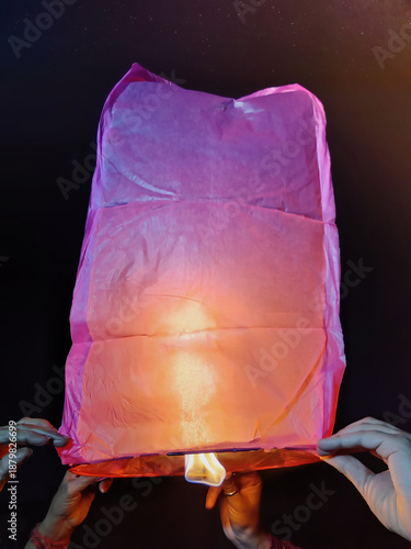 Picture of people holding a sky lantern releasing it at night in dark black sky
