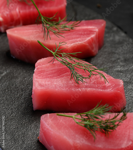 Raw tuna pieces on a black board, decorated with dill sprigs