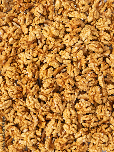 top view of shelled walnut halves scattered across a light pink textured background. The composition is minimalistic, with most walnuts gathered in the lower part of the frame, creating a natural, org