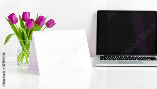 Modern workspace with laptop, blank card, and purple tulip bouquet  