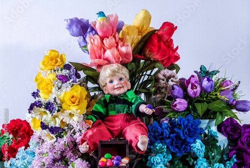 young boy doll sitting on chair in bare feet holding jelly beans in front of spring flowers with white background