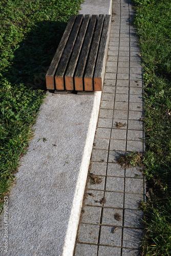 Looking down at a wooden seat on concrete step in a grass park on bright sunny day