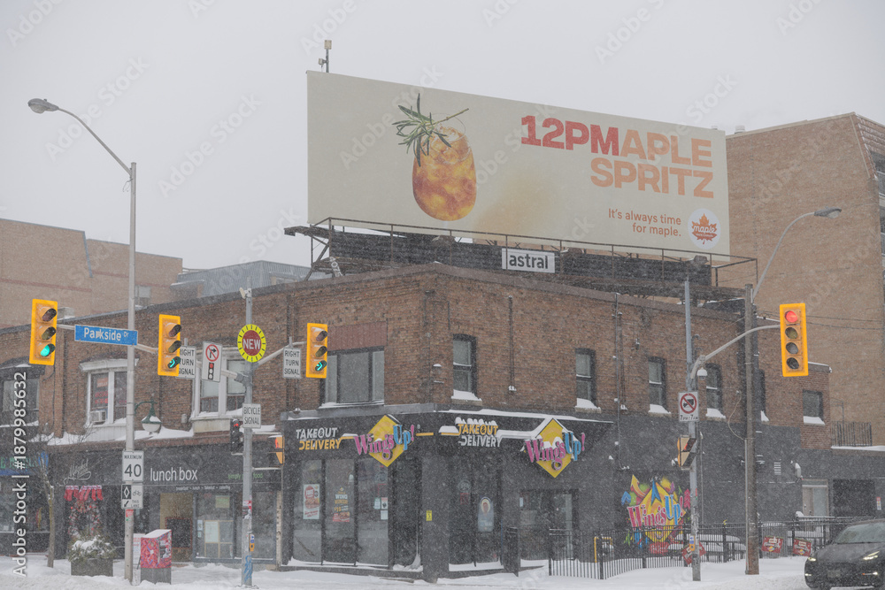 Fototapeta premium looking southeast to corner of Parkside Dr and Bloor St W with rooftop billboard and shop fronts during a snow storm on 2026-01-15 in Toronto