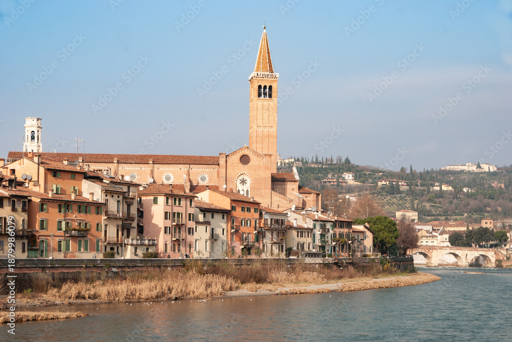 Obraz premium Picturesque view of Verona riverside with colorful houses, church tower and Ponte Pietra over the Adige River, capturing the historic charm of northern Italy.