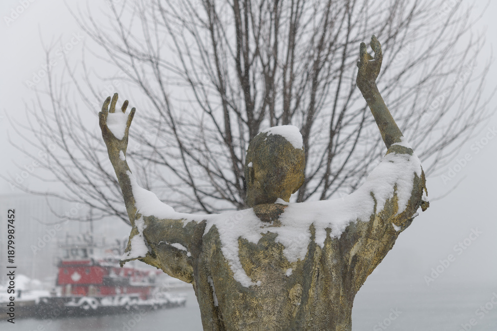 Fototapeta premium The Jubilant Man created by Irish artist Rowan Gillespie part of The Arrival, set beside the old Canada Malting silos on Eireann Quay, Toronto, during winter storm on 2026-01-15