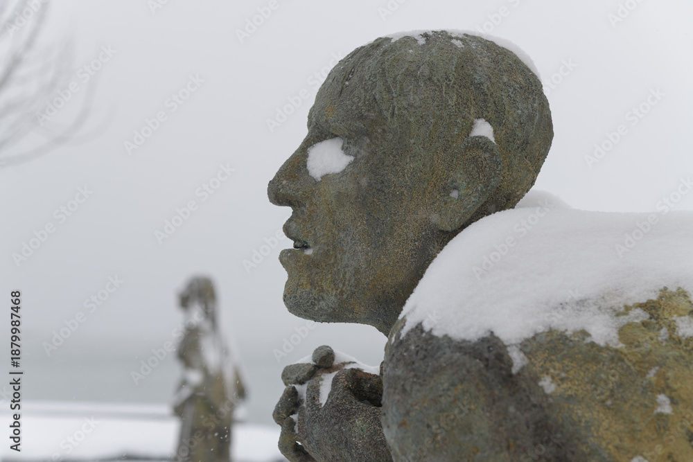 Fototapeta premium left profile of Apprehensive Man created by Irish artist Rowan Gillespie part of The Arrival, set beside the old Canada Malting silos on Eireann Quay, Toronto, during winter storm on 2026-01-15