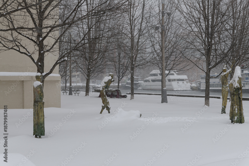 Fototapeta premium wide view of sculptures by Irish artist Rowan Gillespie part of The Arrival, set beside the old Canada Malting silos on Eireann Quay, during winter storm on 2026-01-15 in Toronto