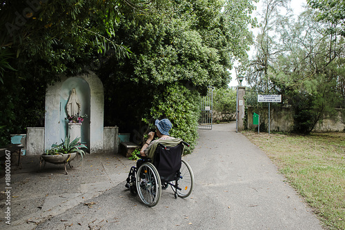 signora in carrozzina prega davanti a  statua della madonna