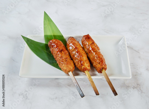 Glazed meat skewers on a white plate with green leaves isolated on marble background