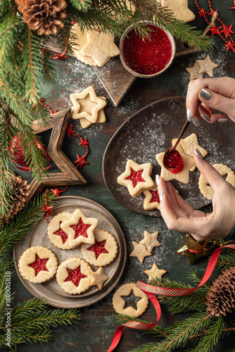 Homemade Linzer Christmas cookies dusted with sugar. Process of filling cookies with ruspberry jam on wooden table, fir tree branches, top view
