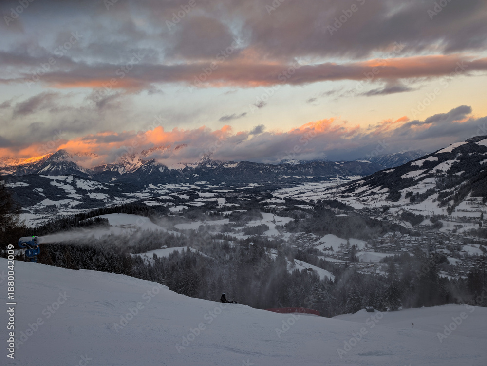 Obraz premium Snow-covered mountain landscape at sunset with a snow machine spraying snow on a ski slope