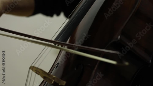 Close up shot of a musician playing the cello. The cellist wears a white shirt and uses a bow on the strings of the classical wooden instrument.

