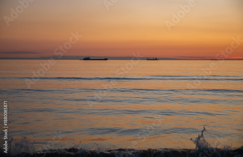 Sunset on a peaceful sea with cargo vessels.