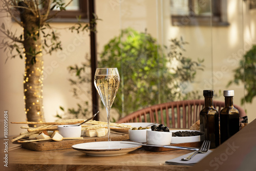 Elegant tall flute of chilled sparkling champagne with different snacks on an elegant formal dining table at outdoor cafe or restaurant in pedestrian street in Europe. Luxury served table at terrace.