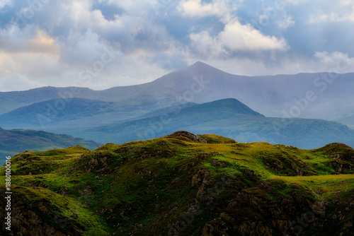 Green hills sit in the foreground, leading back to blue layered mountains. Clouds cover the sky above National Park during the daytime.