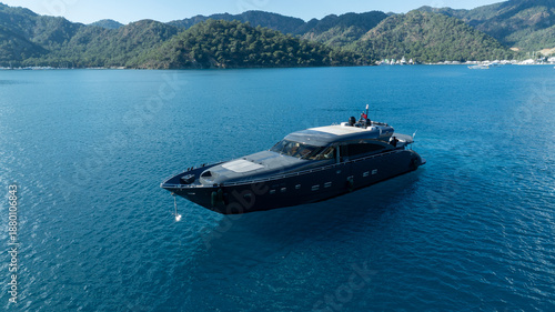 Fotografi Luxury Yacht Sailing in Turquoise Waters: A sleek, modern yacht gracefully navigates the open sea, its dark silhouette contrasting against the vibrant turquoise waters