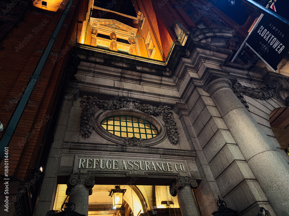 Naklejka premium Manchester clock tower building exterior at night with ornate entrance and Refuge Assurance Co signage