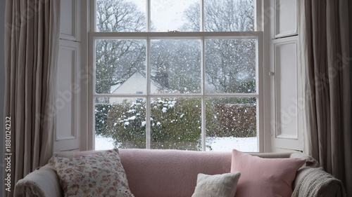 Cozy interior living room overlooking a snowy garden view through a sash window during winter