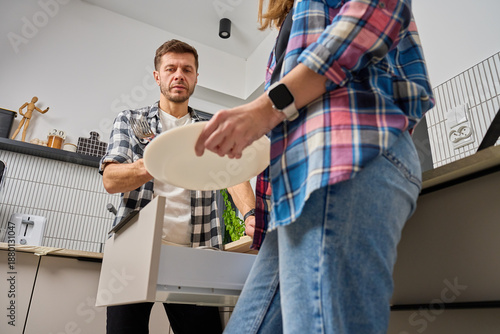 Man and woman standing in kitchen and unloading dishwasher with plates