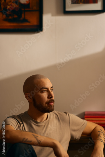 Εκτύπωση καμβά A contemplative man with a beard sits in a warm, indoor setting with dramatic lighting