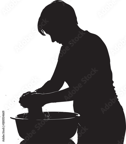 Silhouette of a person hand washing laundry garments in a water basin