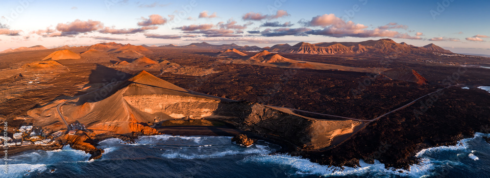 Fototapeta premium Aerial view of Timanfaya National Park on Lanzarote, Canary Islands, with cinder cones, lava fields, El Golfo and Los Hervideros coast, ribbon road, and Ajaches ranges at sunrise.