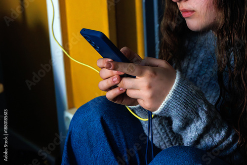 Close up of young woman hands holding and using smartphone with charging cable in the hotel room
