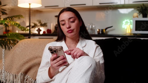 Young woman scrolls news at night home bored tired looks at smartphone sighs stressed unmotivated. Caucasian girl on sofa at evening shows fatigue burnout mood dull scroll stare poor focus wants rest.