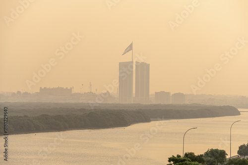 Ras Al Khaimah, UAE, 12.10.2025. City skyline with tall buildings and Uae flag near river during foggy morning in urban area.