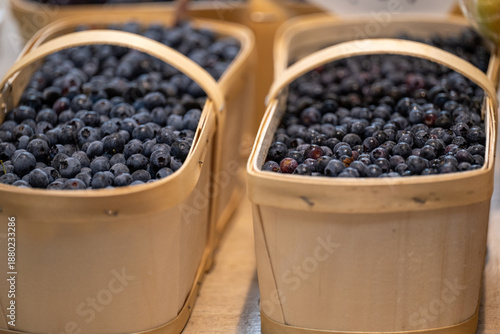 Multiple large wooden baskets with handles are filled with wild blueberries for sale at a farmers' market. The fruits are antioxidant berries with a dark blue and purple tint. The harvest is organic. 