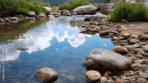 Clear brook reflecting blue sky and clouds over smooth pebbles and rocks