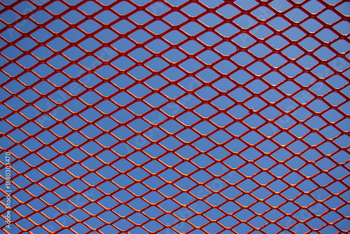 Close-up of Red Metal Diamond Pattern Fence Against Blue Sky