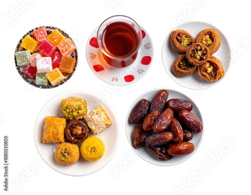 Minimalist top view of dates, mixed sweets, traditional tea glass and decorative fanous, isolated on white background