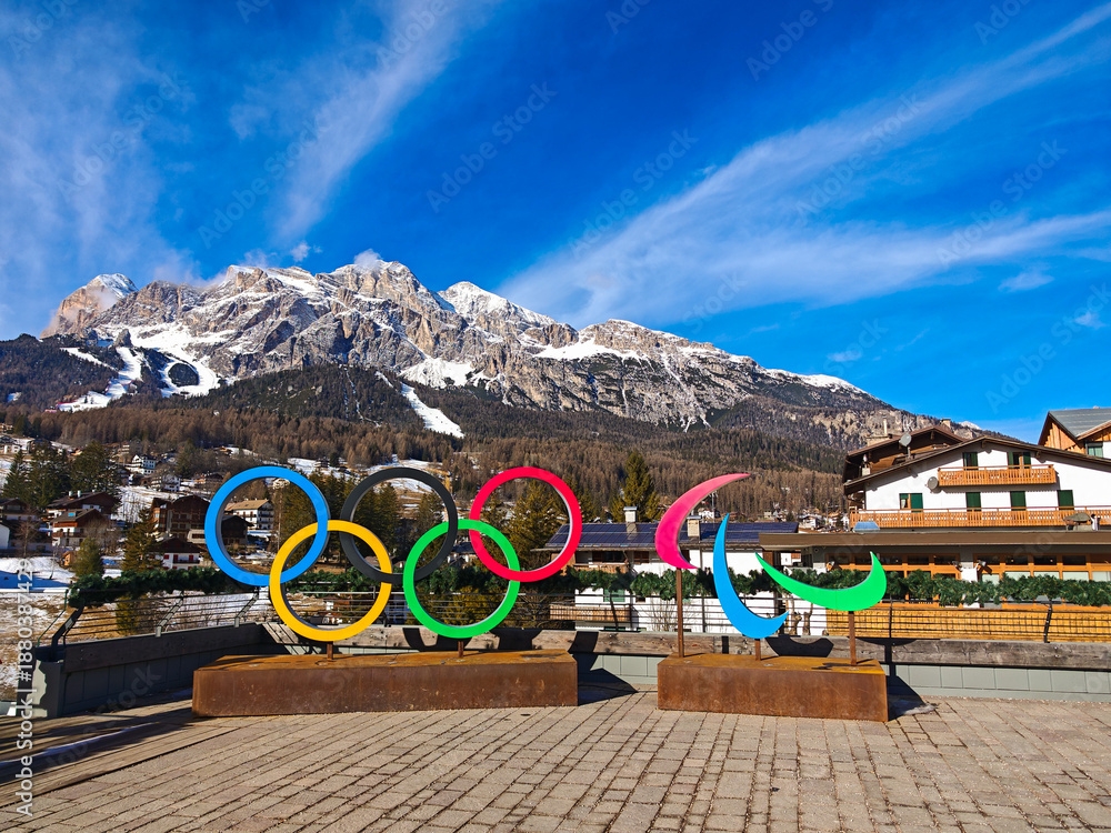 Fototapeta premium CORTINA D'AMPEZZO, ITALY - JANUARY 22, 2025: Vibrant Olympic Rings installation in Cortina d'Ampezzo with the snow-covered Italian Dolomites mountains in the background under a blue sky