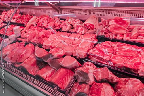 Chilled fresh meat on display with red lighting. Fresh cuts of beef and pork are organized in a meat display case at a local shop. The vibrant red meat is visible under bright lights. High quality