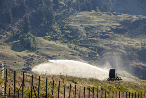Agricultural water wheel hose reel irrigation system in use spraying water to irrigate grapes or other crops in agriculture farming for food in the hillside country landscape
