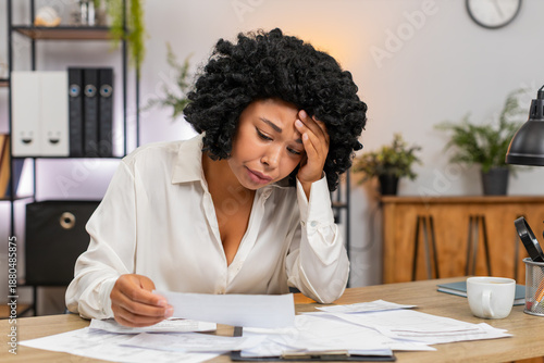 African American businesswoman at home office studies overdue bills fearing debt and high taxes. Freelancer girl at table counts receipts invoices seeking cuts to protect savings and avoid bankruptcy