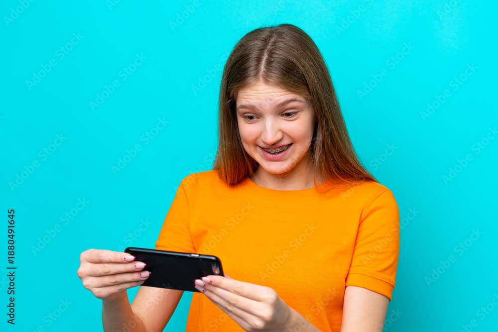 Naklejka premium Teenager Russian girl isolated on blue background playing with the mobile phone