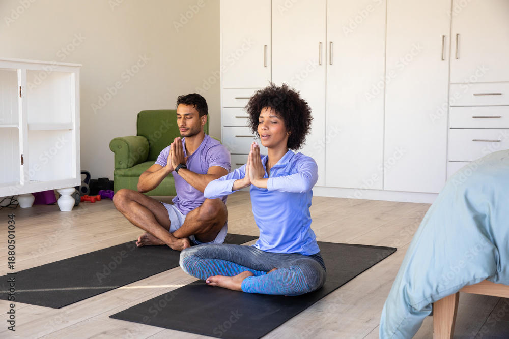 Obraz premium Diverse couple meditating on yoga mats in sportswear in bedroom with cabinets, armchair