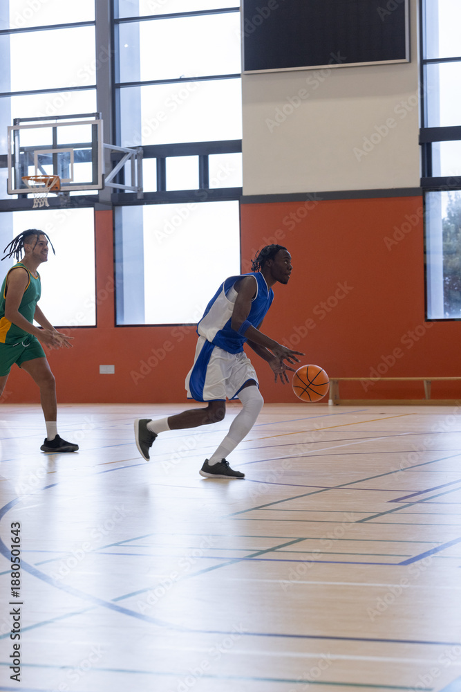 Obraz premium Diverse male basketball players in jersey dribbling and defending at gym court with hoop bench