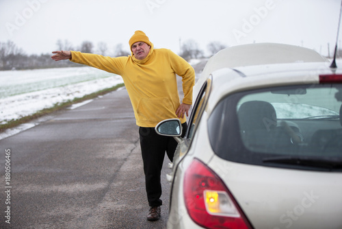 Canvas-taulu Man in yellow hoodie signals for help beside a broken-down car on a rural road d