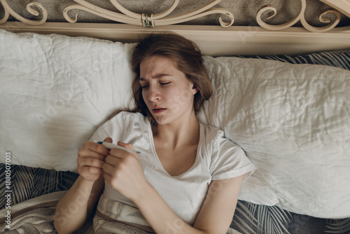 Young woman has flu catarrh ill sick disease treatment cold check measures temperature thermometer lay in bed