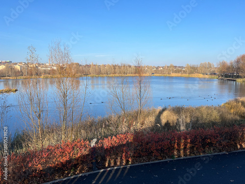 Calm lake stretches under a clear blue sky, surrounded by bare trees and soft autumn colors. Ukraine, Bucha region