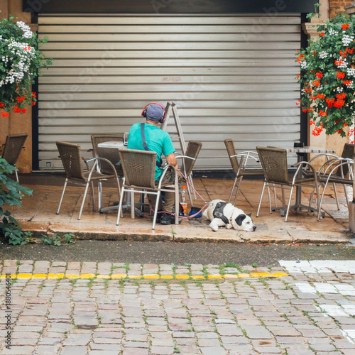 Un homme assis sur une terrasse de café avec son chien en laisse.
Scène de vie en ville.