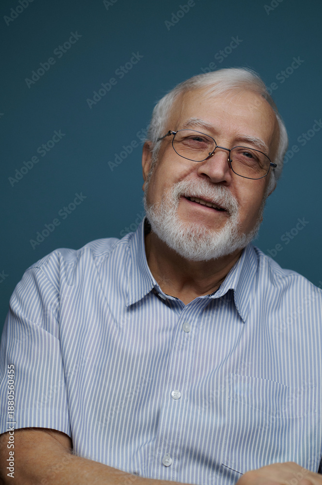 Obraz premium Elderly man smiles while sitting against a blue wall in a bright room during daytime